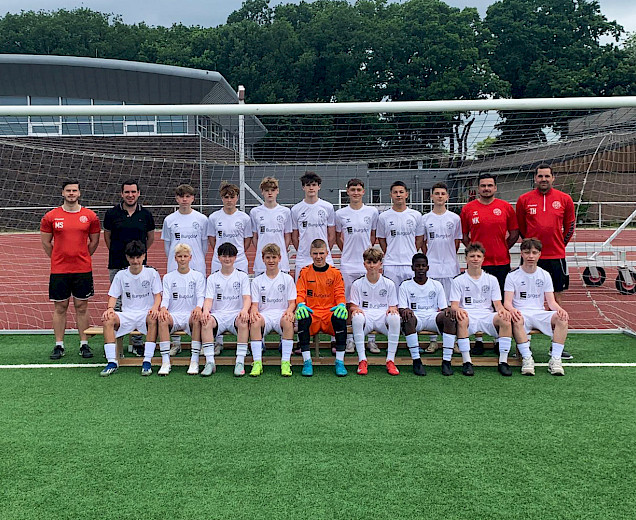 Mannschaftsfoto mit Fußballspielern in den neuen weißen Trikots und den Trainern, die dem Sponsor ein Geschenk überreichen