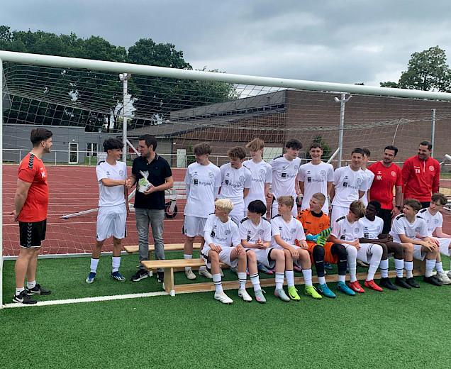 Übergabe des Geschenks an den Sponsor Mathias Burgdorf durch einen Spieler, die Mannschaft sitzt im Hintergrund