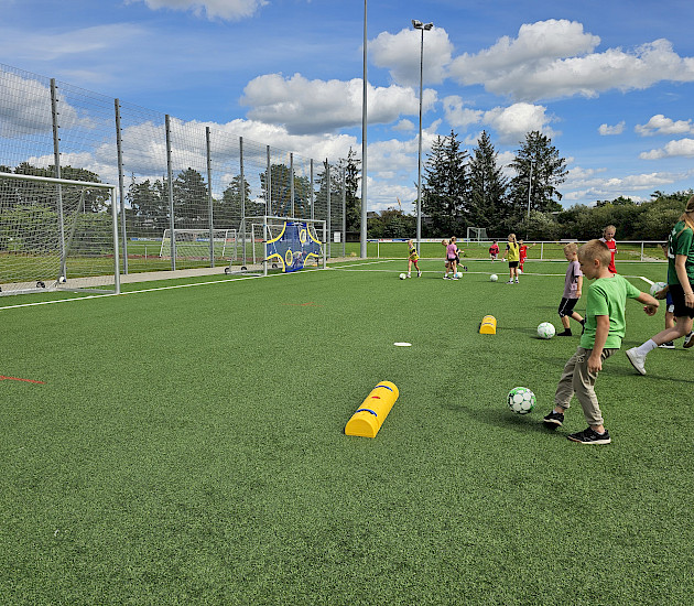 Kinder, die beim polysportiven Camp bei Sonnenschein Fußball spielen auf dem Kunstrasen