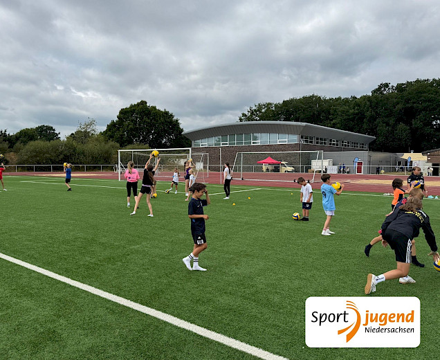 Kinder, die beim polysportiven Camp bei Sonnenschein Fußball spielen auf dem Kunstrasen
