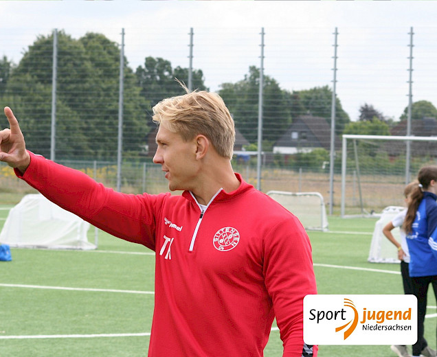 Trainer Tom beim Camp, der den Kindern etwas sagt und mit dem Arm in eine Richtung deutet