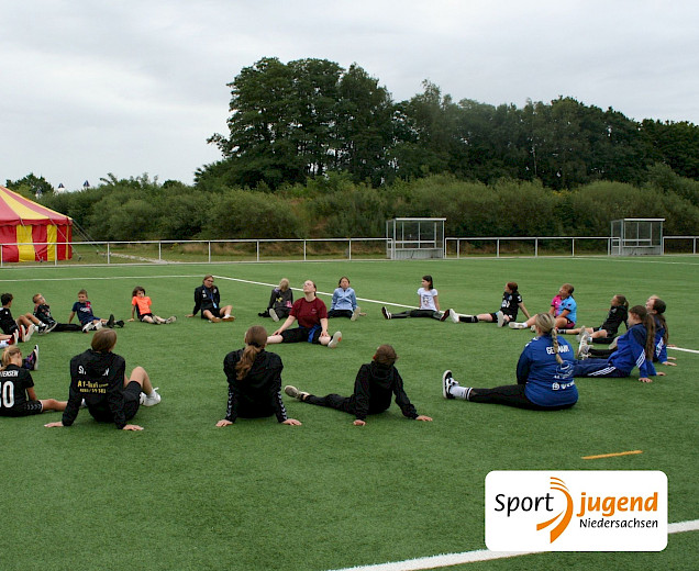 Kinder sitzen im Kreis un die Trainerin vom Linedance sitzt in der Mitte. Sie machen eine Dehnübung
