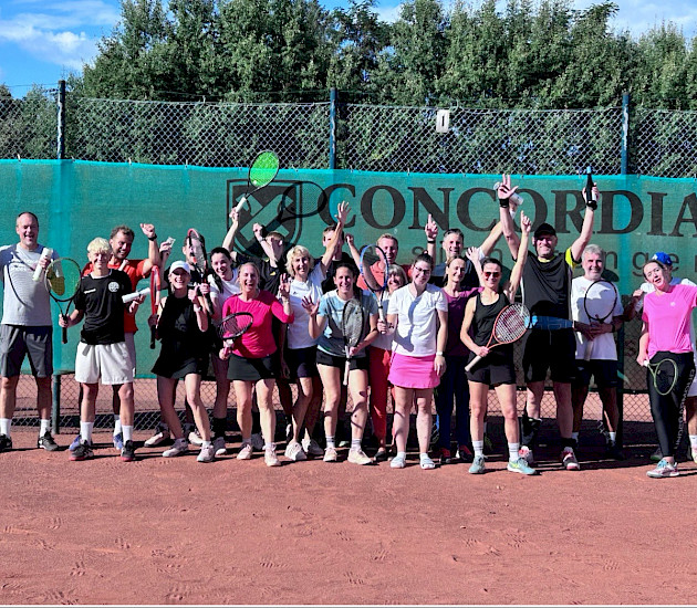 Tennisgruppe, die beim Jubiläum zusammensteht und alle haben die Arme nach oben, weil sie sich freuen