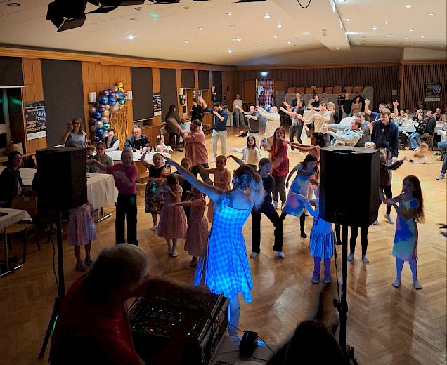 Viele Menschen in einem Raum bei der Inklusionsdisko, die gemeinsam feiern und alle die Arme hochnehmen zum gemeinsamen Tanz