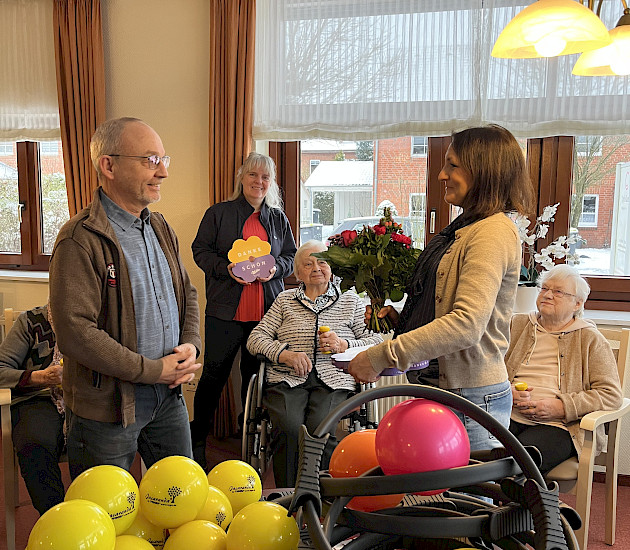 Übergabe einen Blumenstrausses an die Pflegedienstleitung vor Sportgeräten