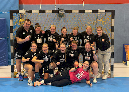Handball-Damen-Team steht mit ihrem Trainer im Tor und bejubeln den Sieg