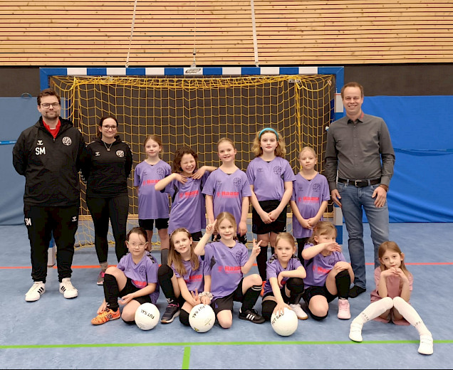 Die F-Mädchen sitzen zusammen und der Sponsor und der Trainer stehen links und rechts neben ihnen. sie freuen sich über die neuen Trikots Die F-Mädchen sitzen zusammen und der Sponsor und der Trainer stehen links und rechts neben ihnen. sie freuen sich über die neuen Trikots