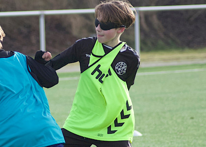 Auf dem Fußballplatz spielen 2 Jungs Fussball, beide tragen Leibchen und eine Verdunklungsbrille aus dem neurozentrierten Training