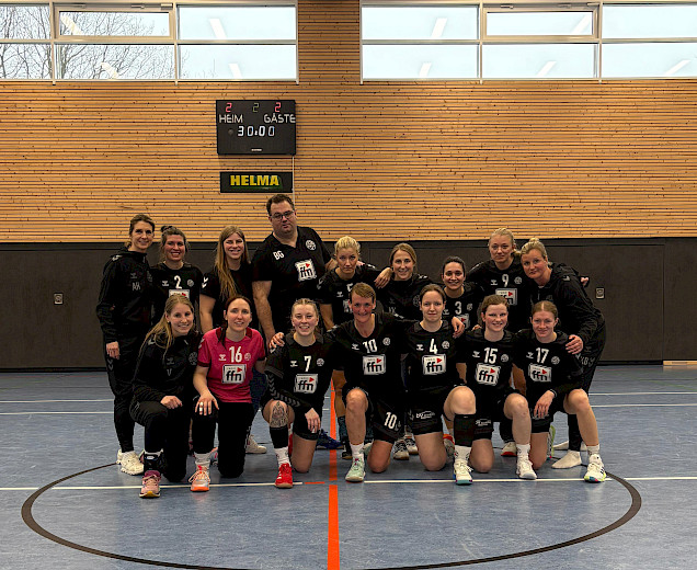 In der Halle hocken die Damen in 2er Reihe zusammen und der Trainer steht hinten in der Mitte