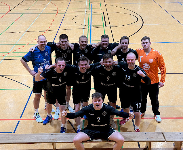 Das Foto ist von oben auf die Handballer in der Halle herunterfotografiert, die sich in 2 Reihen für das foto aufgestellt haben. Ganz vorn sitz ein Spieler auf der Bank