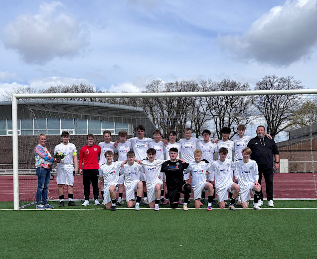 Birgit Rethejn-sTemman steht lins neben den Fußballern, die sich für das neue Trikot in Weiß mit dem Logo von VGH darauf bedanken. sie hält einen Blumenstrauß in der Hand.