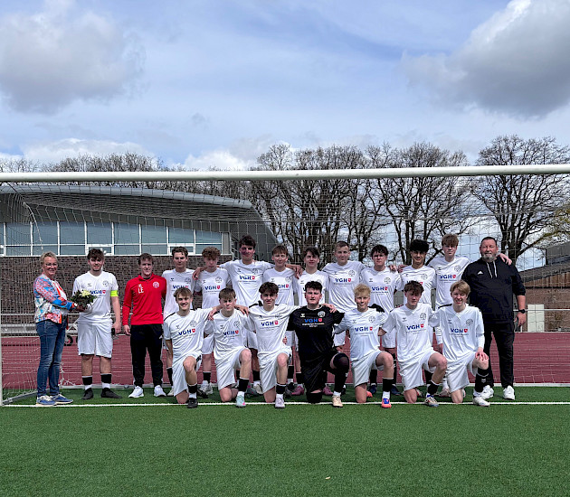 Birgit Rethejn-sTemman steht lins neben den Fußballern, die sich für das neue Trikot in Weiß mit dem Logo von VGH darauf bedanken. sie hält einen Blumenstrauß in der Hand.