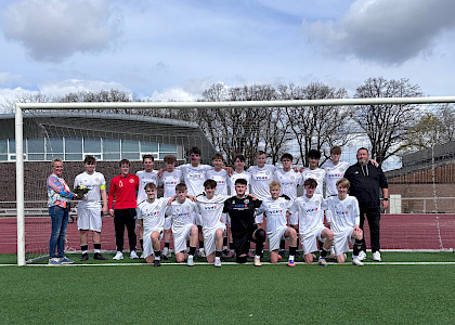Birgit Rethejn-sTemman steht lins neben den Fußballern, die sich für das neue Trikot in Weiß mit dem Logo von VGH darauf bedanken. sie hält einen Blumenstrauß in der Hand.