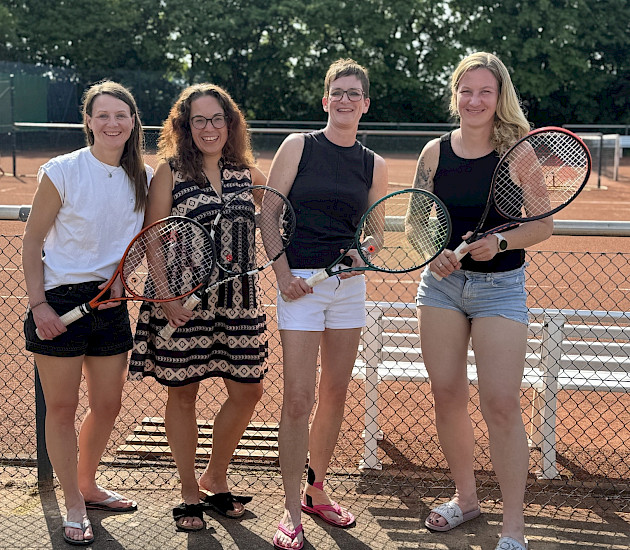 vier Tennisspielerinnen stehen nach dem Sieg fürbass Foto mit ihren Schlägern in der Hand vor dem Tennisplatz