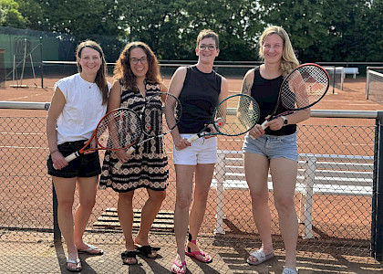 vier Tennisspielerinnen stehen nach dem Sieg fürbass Foto mit ihren Schlägern in der Hand vor dem Tennisplatz